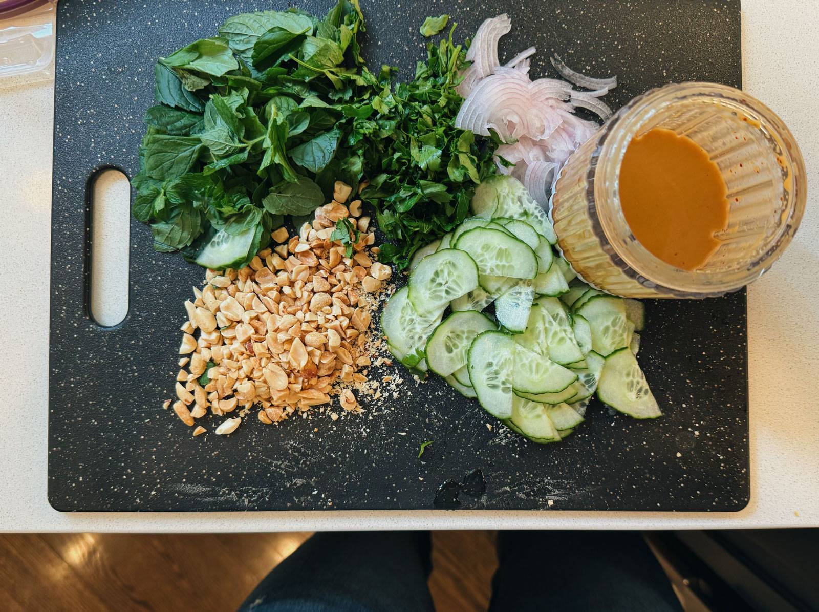 Chopped herbs, peanuts, shallots, and cucumber on a cutting board with a jar of dressing.