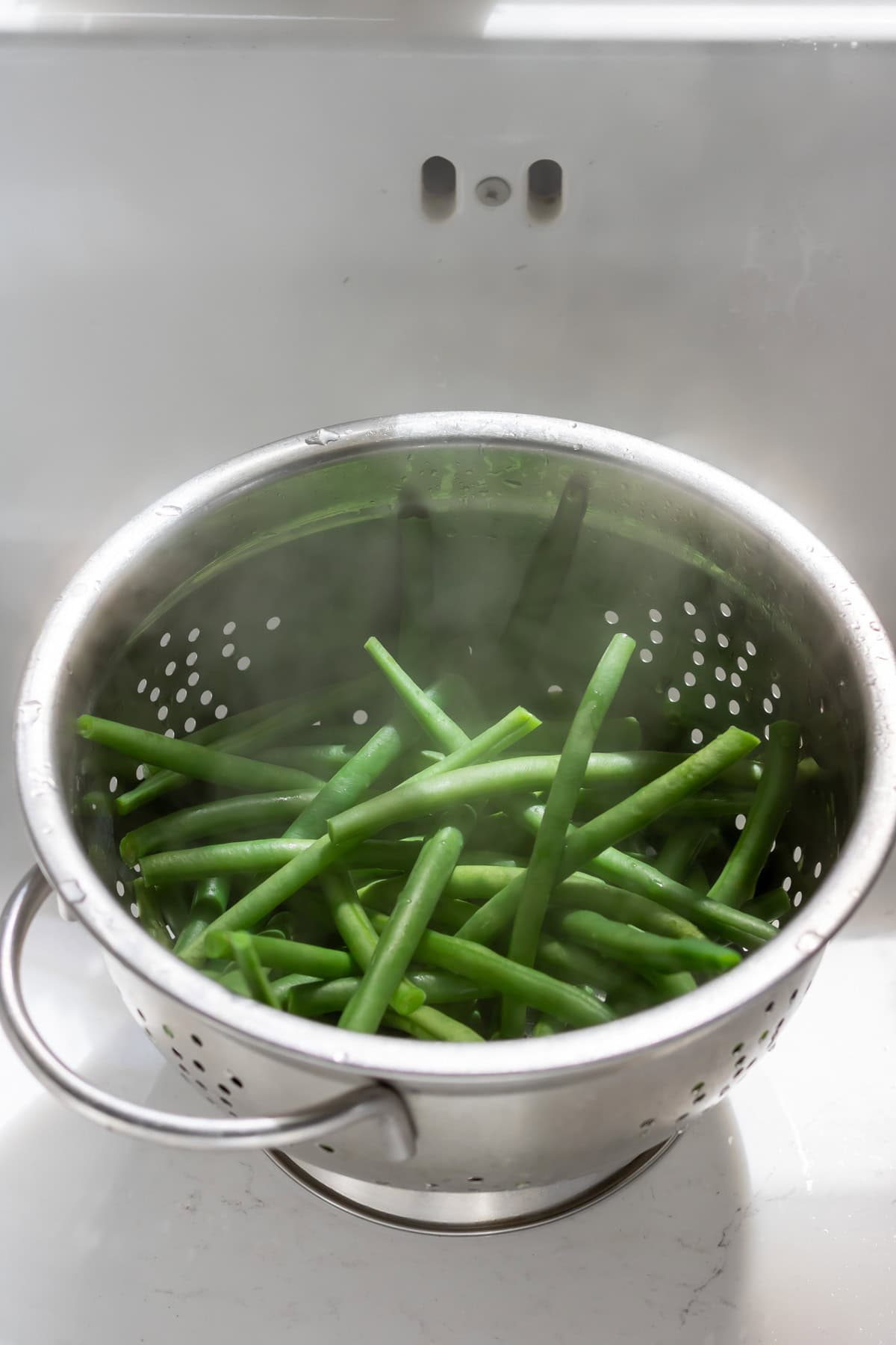 Draining green beans in a colander in the sink.