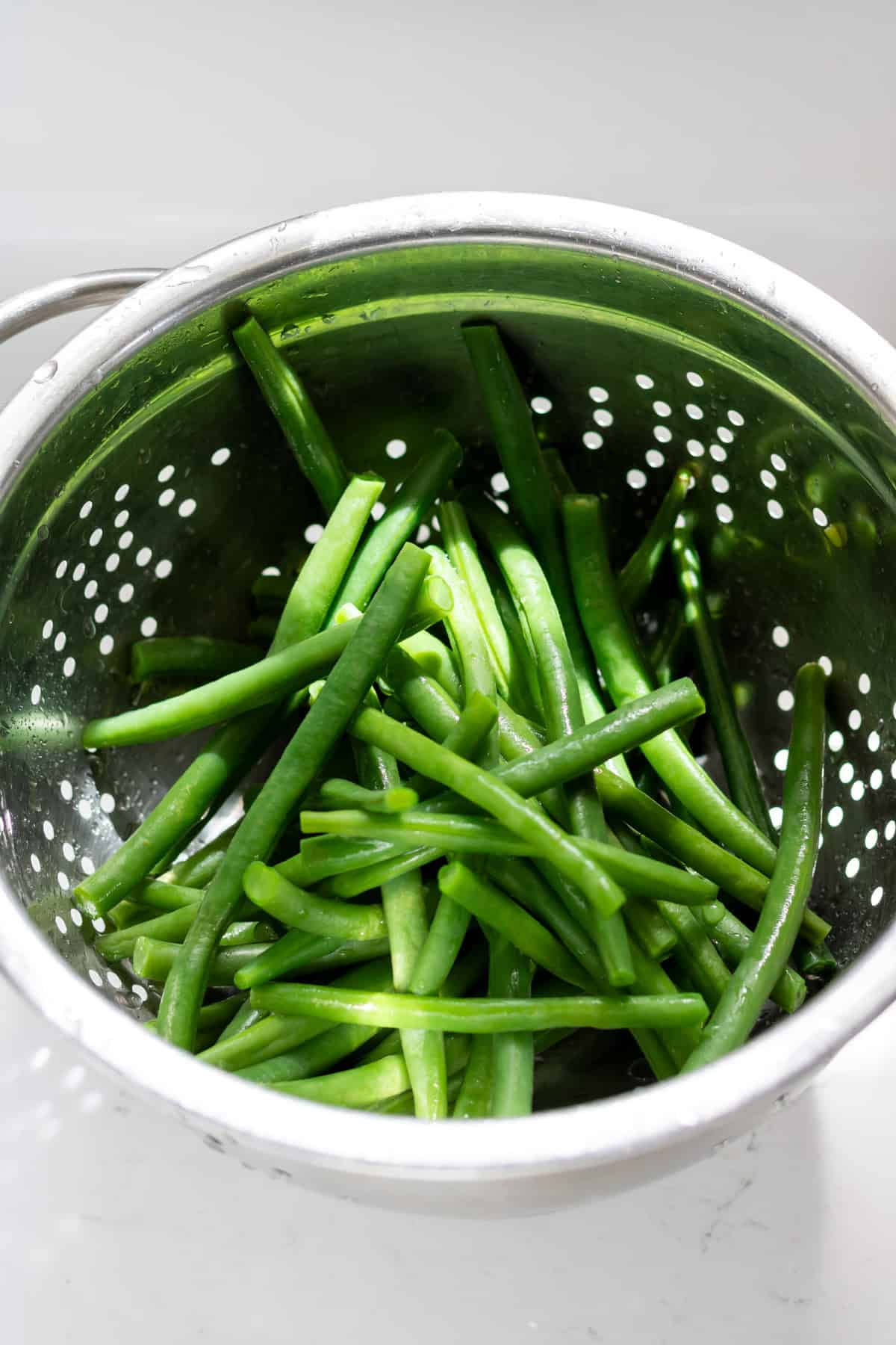 Drained cold blanched green beans in a colander.