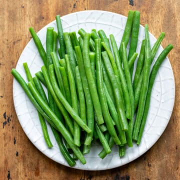 A wooden table with a plate of blanch green beans.