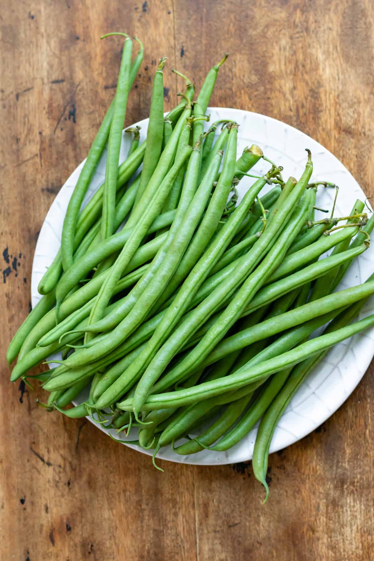Fresh untrimmed green beans on a plate on a wooden table.