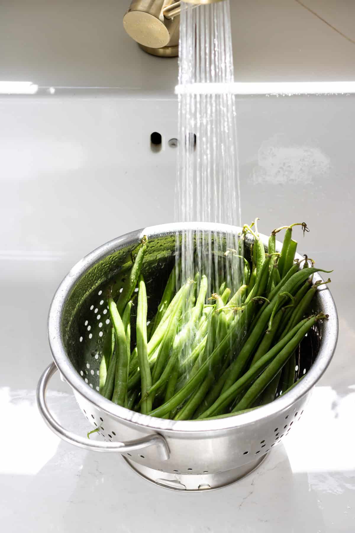 Rinsing green beans in a colander in a sink.