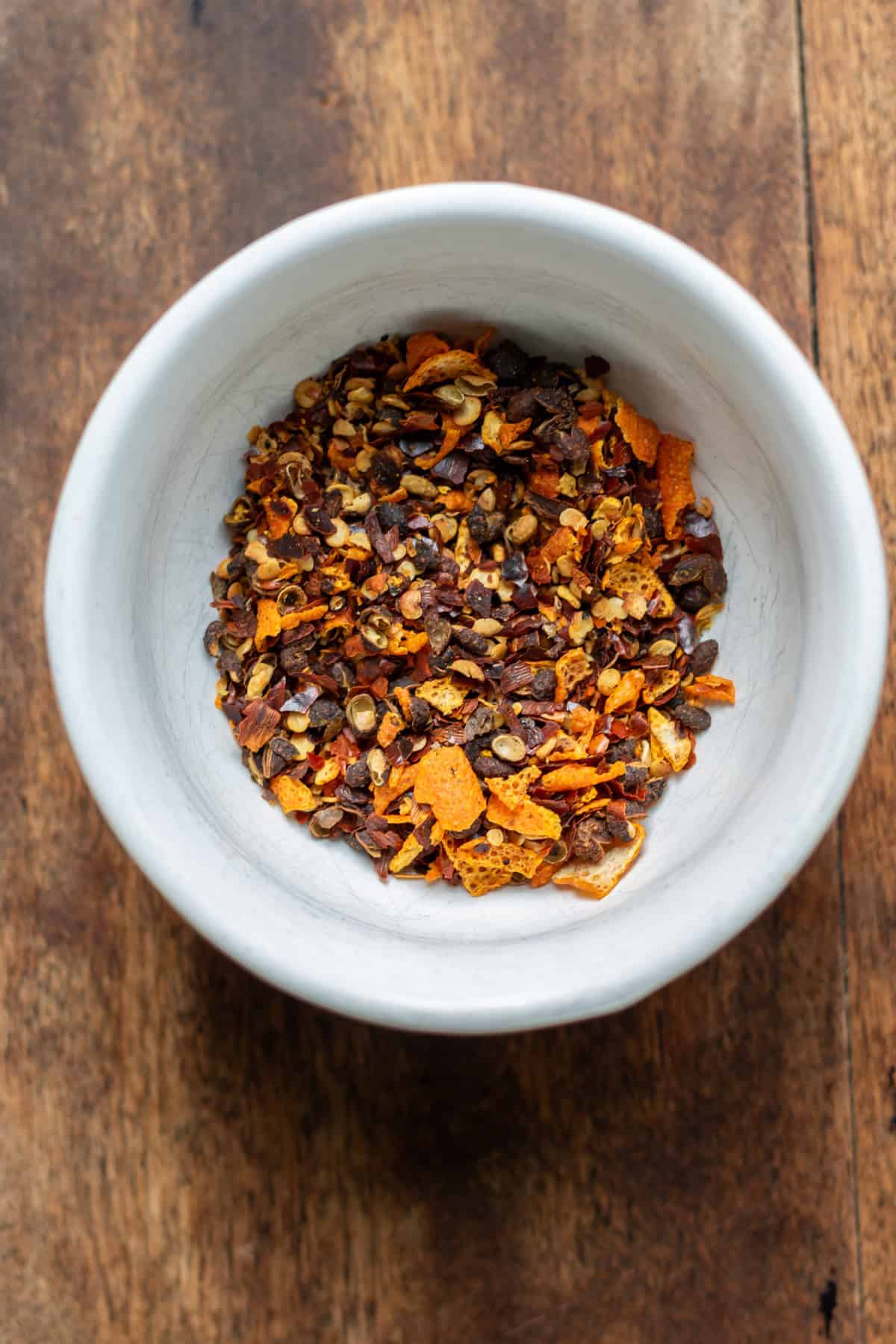 Peppercorns, chili flakes and dried orange peel in a dish.