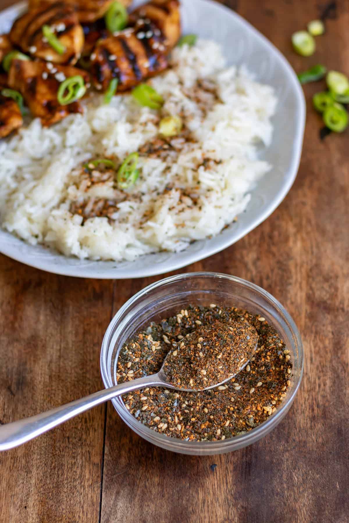 Spoon in a dish of shichimi togarashi, next to a plate of rice with some sprinkled on it.