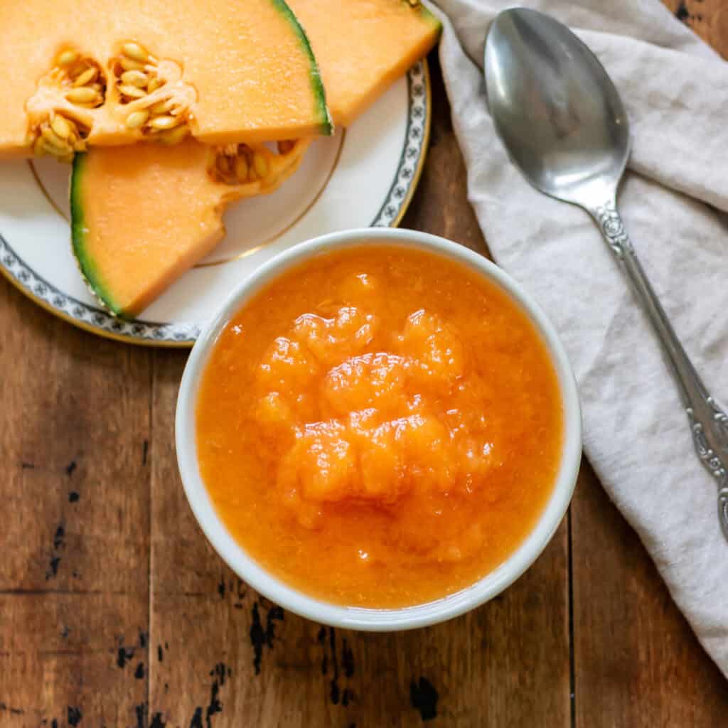 Dish of melon compote in front of a plate with slices of cantaloupe.