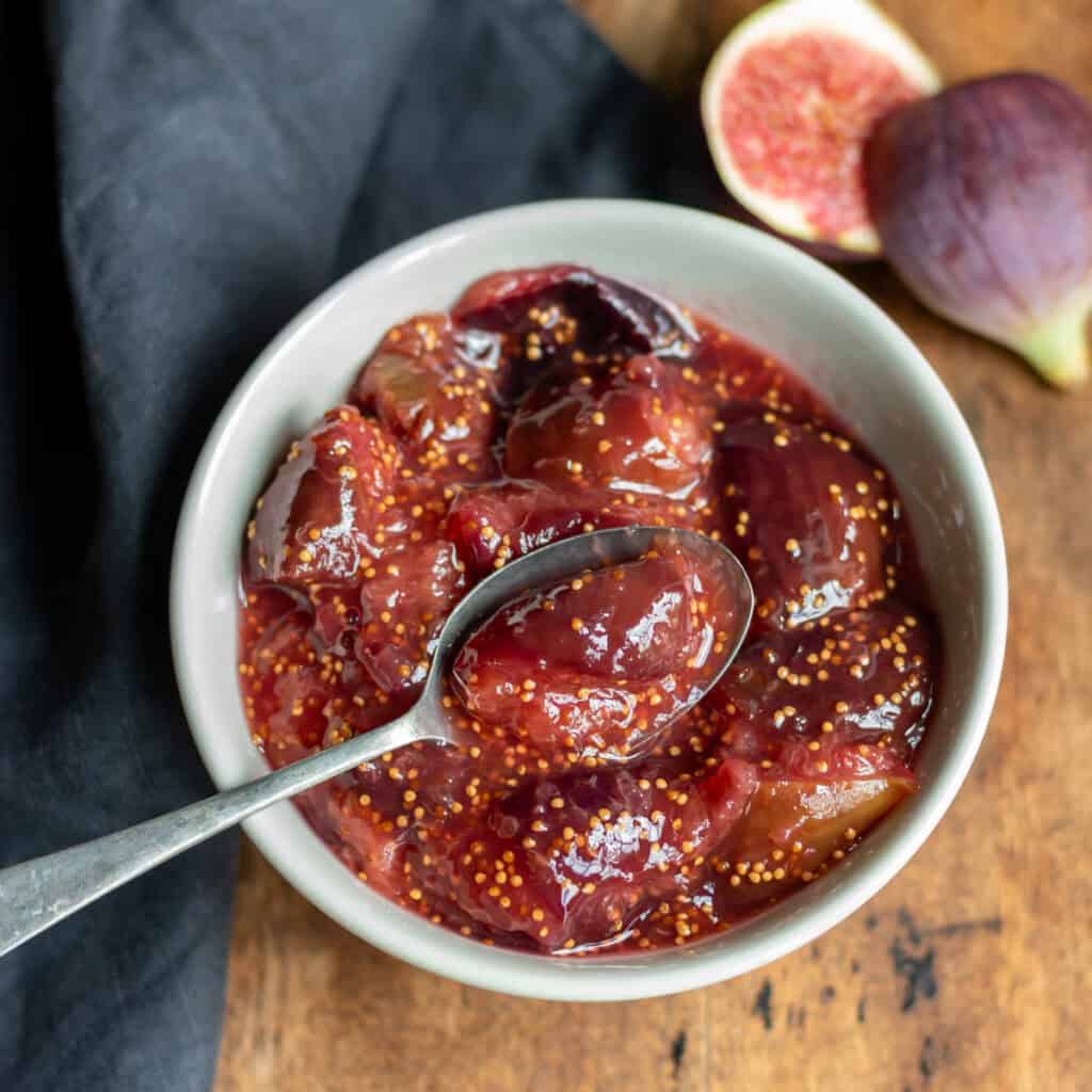 Wooden table with a bowl of fig compote next to a fresh fig.