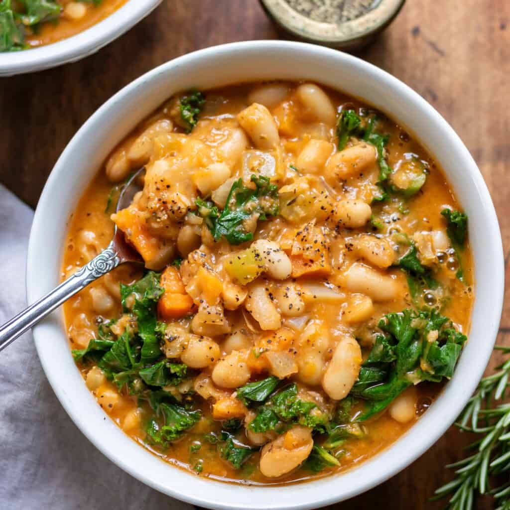 Close up of a spoon in a bowl of kale and white bean soup.