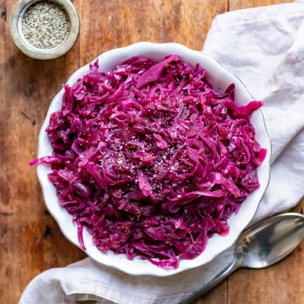 Looking down at a serving dish of braised red cabbage on a wooden table.